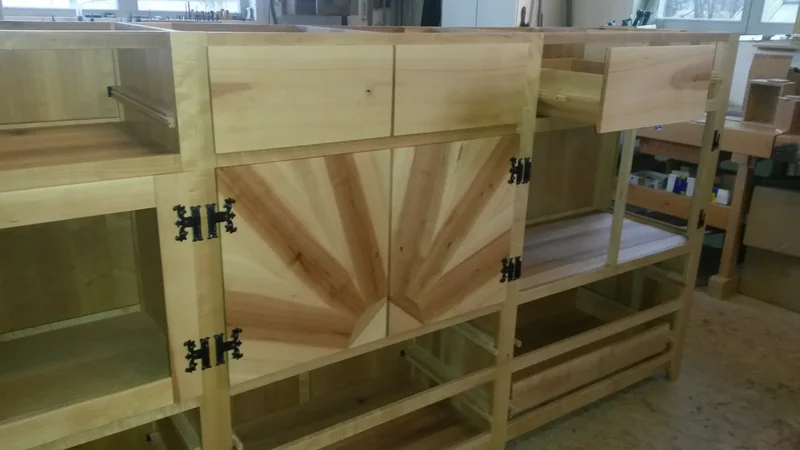 Anrichte im Rohbau in der Werkstatt: offene Korpusse, ein Türfeld mit strahlenförmig aufgebauter Maserung, schwarze Schmiedebänder.